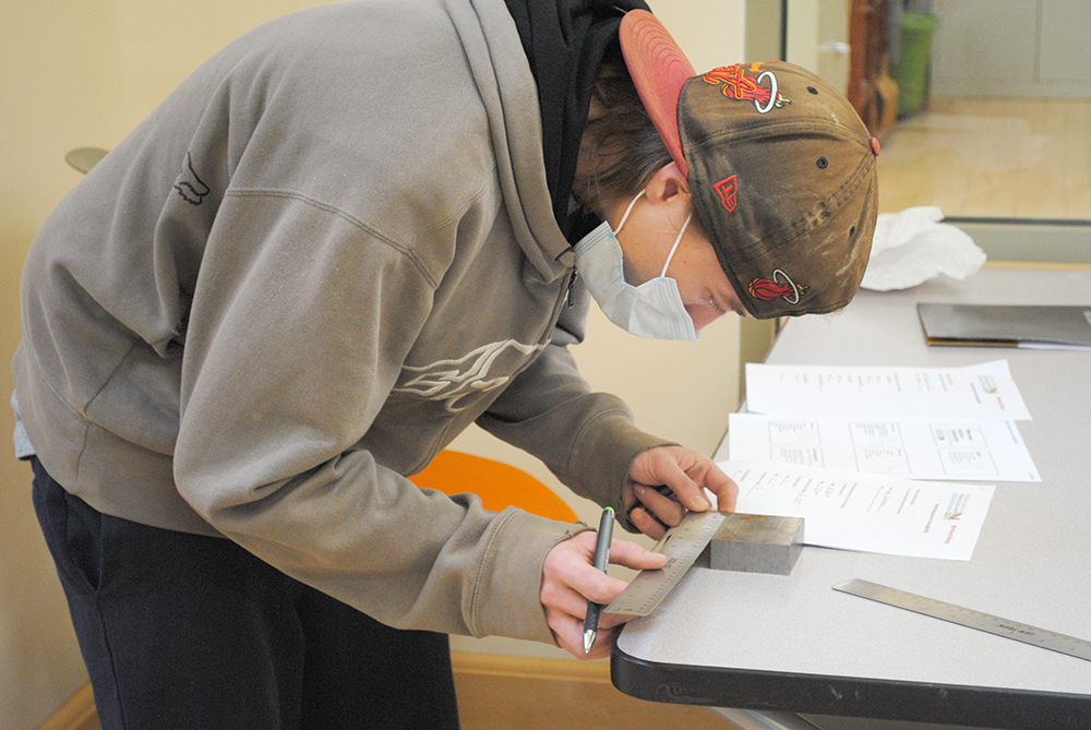 Hitachi ABB new hire Ian Shumate completes a hands-on lab assignment using a straight-edge metal ruler to measure a thick metal block.