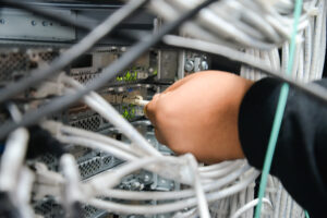 A hand plugging in a cable to the back of a server