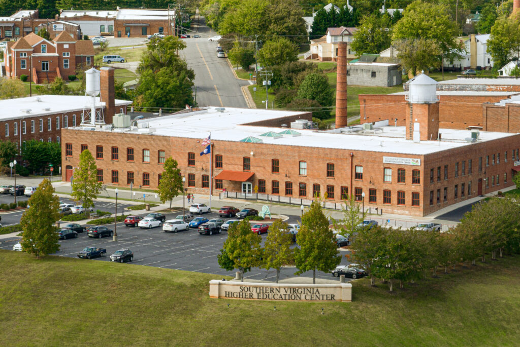 An aerial photo of the Southern Virginia Higher Education Center's 820 Bruce Street Building with the SVHEC sign, three trees, and the parking lot with cards in the foreground.