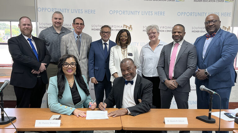 Dr. Charlette Woolridge (front, left) and Southside Virginia Community College president Dr. Quentin Johnson (front, right) are seated at a table with SVHEC Board of Trurstees' members standing behind and around them. The photo was taken to highlight the MOU signing between SVHEC and SVCC to provide expanded access to SVHEC's HVAC training program.